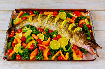 Fresh pike with lemon and vegetable in baking pan.
