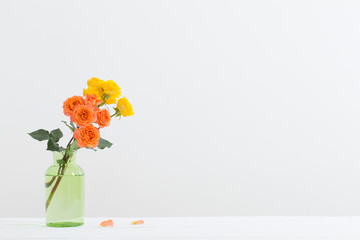 orange and yellow roses in glass vase on white background