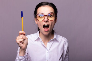  girl in a white shirt and glasses holds a pen with her mouth