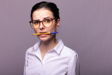  girl in a white shirt and glasses holds a pen with her mouth