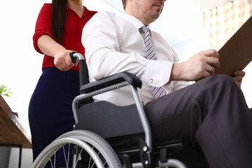 Fototapeta na wymiar Close-up of woman co-worker accompany man in disabled carriage. Employee reading important papers. Business and adaptation of people with disabilities in society concept