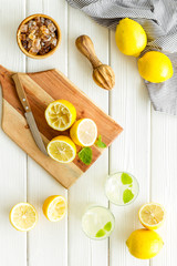 Homemade lemonade in glasses near juicer and cut lemons on white wooden background top-down