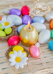 Fototapeta na wymiar Greeting card Easter burning golden candle and chocolate eggs in colored foil. Evening. Daisy flower