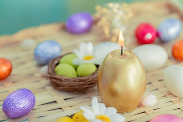 Obraz na płótnie Canvas Greeting card Easter burning golden candle and chocolate eggs in colored foil. Festive easter concept. Daisy flower