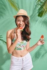Fashion pretty asian woman is eating a slice of watermelon in the  blue background
