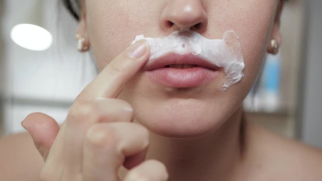 Shaving female mustache concept. Young attractive caucasian girl smears shaving foam on her face with her fingers. Close-up