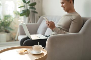 Man using smartphone and laptop on sofa