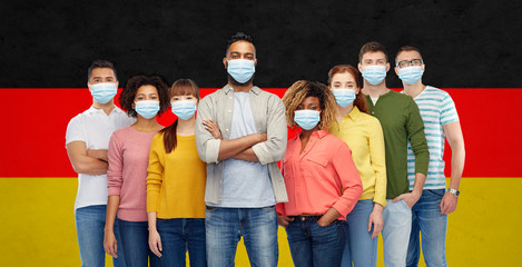 Obraz premium health, safety and pandemic concept - group of people wearing protective medical masks for protection from virus over german flag background