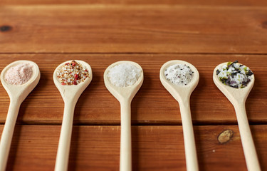 food, culinary and unhealthy eating concept - spoons with salt and spices on wooden table