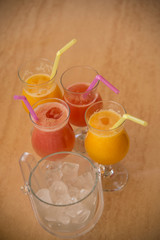 Four glasses of fresh fruit juices with straw and a glass of ice cubes