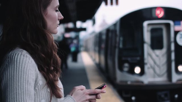 Young adult woman subway platform holding mobile phone