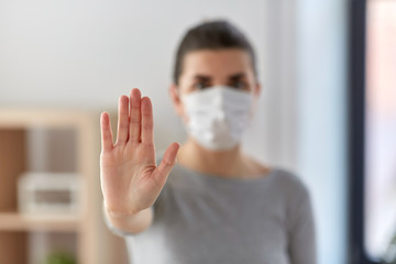 health, safety and pandemic concept - young woman in protective medical mask making stop gesture at...