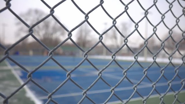 A Wide Metal Of Fence Of Blue Painted Tennis Court Surrounded With Trees. -medium shot