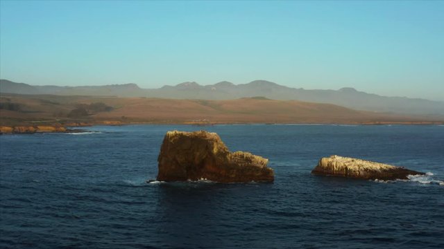 Aerial drone parallax shot of rocks in the middle of the ocean off of the coast of San Simeon, California, USA