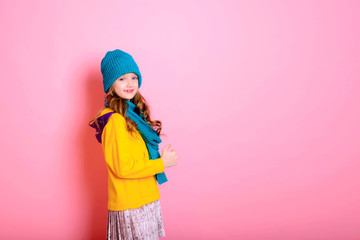 Blonde kid child girl is dressed in a warm sweater, scarf and beanie on a pink background. Fight the cold. Winter and autumn seasons. Concept of children's health, vitamins, medicines.