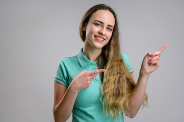 Photo of a pretty girl with long hair in a turquoise t-shirt on a white background. Model shows her hands to the sides, demonstrating the beauty of a smile