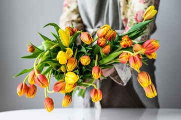 The concept of the florist's work. A girl makes a bouquet of yellow, orange and red Tulips. White background