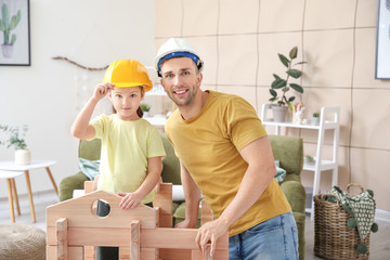 Father and little daughter dressed as builders playing with take-apart house at home