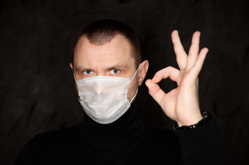 Portrait of a man in a medical mask shows his fingers on a black background