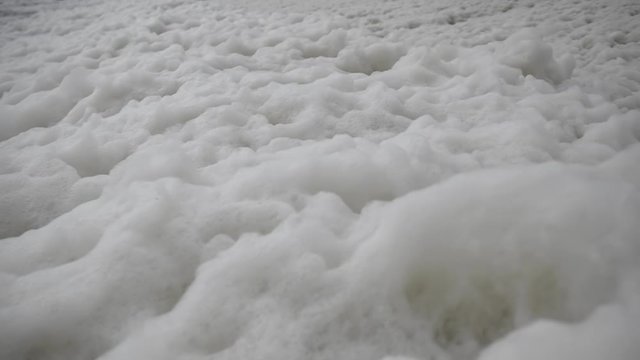 Ecology, a sea of ​​white foam on the seashore is blown away by the beach.