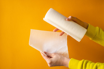 female hand holds a roll of white paper towels on a yellow background, horizontal frame, copy space, close-up