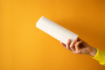 female hand holds a roll of white paper towels on a yellow background, horizontal frame, copy space, close-up