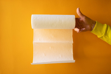 female hand holds a roll of white paper towels on a yellow background, horizontal frame, copy space, close-up