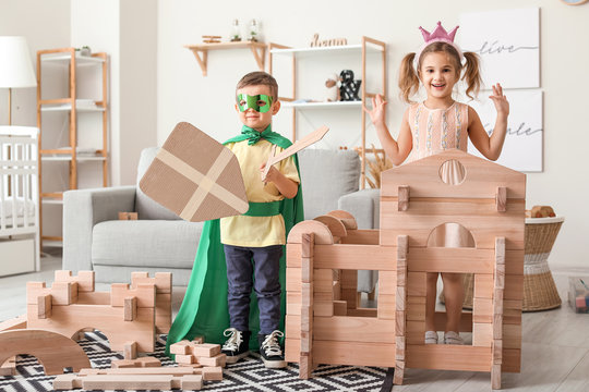 Little children in costumes playing with take-apart house at home