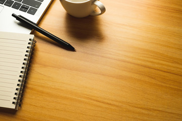 Desk with laptop, pen and blank notepad on wood table.