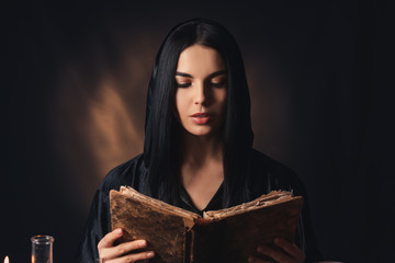 Female alchemist with book on dark background