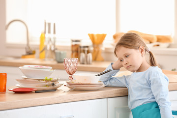 Fototapeta na wymiar Reluctant little girl looking at dirty dishes in kitchen