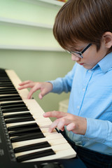 boy with glasses learns to play the synthesizer.