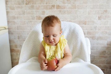 Adorable baby holding apple on table of feeding chair and smiling