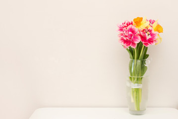 Beautiful spring tulips in vase on table against light background with a copy space