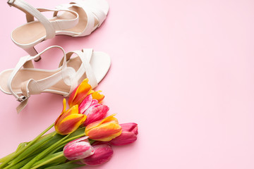 Women flat lay with sandals and bouquet of tulips on pink background with a copy space