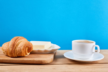 Coffee breakfast with croissant, butter and cup of black coffee on a oak wooden table.