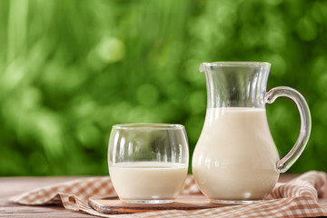 Glass and jug of fresh milk on table outdoors