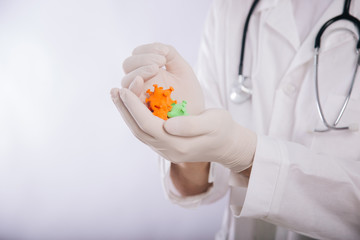 A doctor in a white coat and gloves on a white background holding a mock coronavirus in his hands. Shows a multi-colored virus. Male paramedic in a medical mask