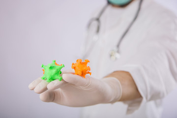 A doctor in a white coat and gloves on a white background holding a mock coronavirus in his hands. Shows a multi-colored virus. A male paramedic in a medical mask contracted a dangerous disease