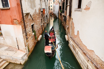 Scene with traditional gondola and canal in Venice, Italy. A man in the gondola near old houses