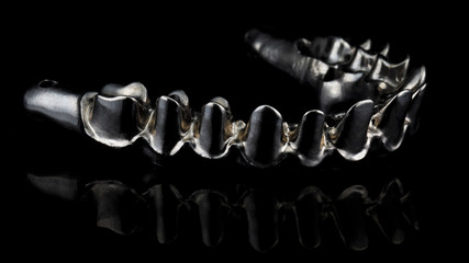 macro photo of an excellent titanium beam to create an upper jaw prosthesis, side view on a black background © Dental Pro Content