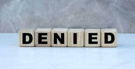 The concept of the word DENIED on cubes on a gray background