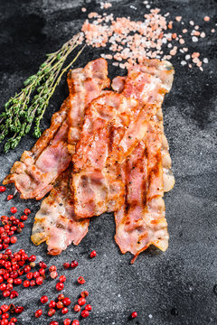 Cooked sizzling hot tasty crispy bacon. Black background. Top view