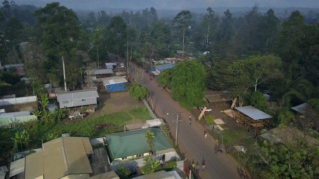 Aerial view moving right shot, people walking on the road passing by each other, scenic view houses and palm trees in the background in Goroka, Papua New Guinea