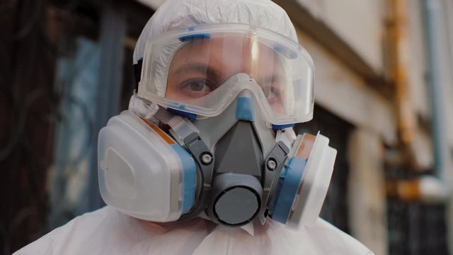 Close up of virologist medical worker in protective hazmat, goggles and respirator in background of building