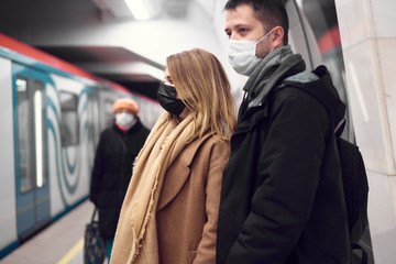 Man and woman in medical masks standing near car in subway.