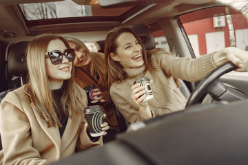 Girls inside the car. Women with a coffee. Friends have fun in a car.