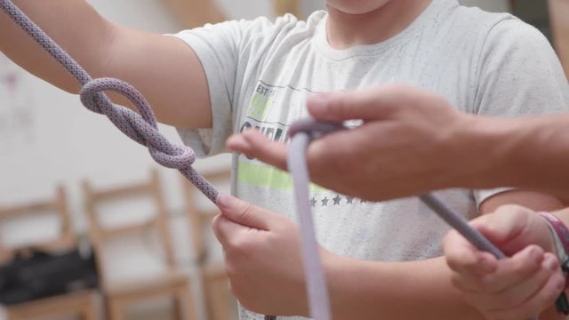 Teacher is giving advice to a child how to tie a knot for climbing