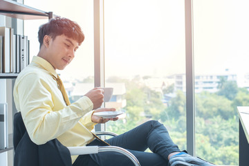 Happy young asian businessman in formal drink coffee sitting in modern workplace in break time