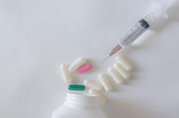 White and green pill capsules on white background near syringe and white pill bottle